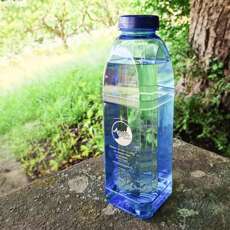 Eine mit Wasser gefüllte blaue Tritan Trinkflasche 8-Kant mit dunkelblauem Schraubdeckel auf einem Stein im Wald.