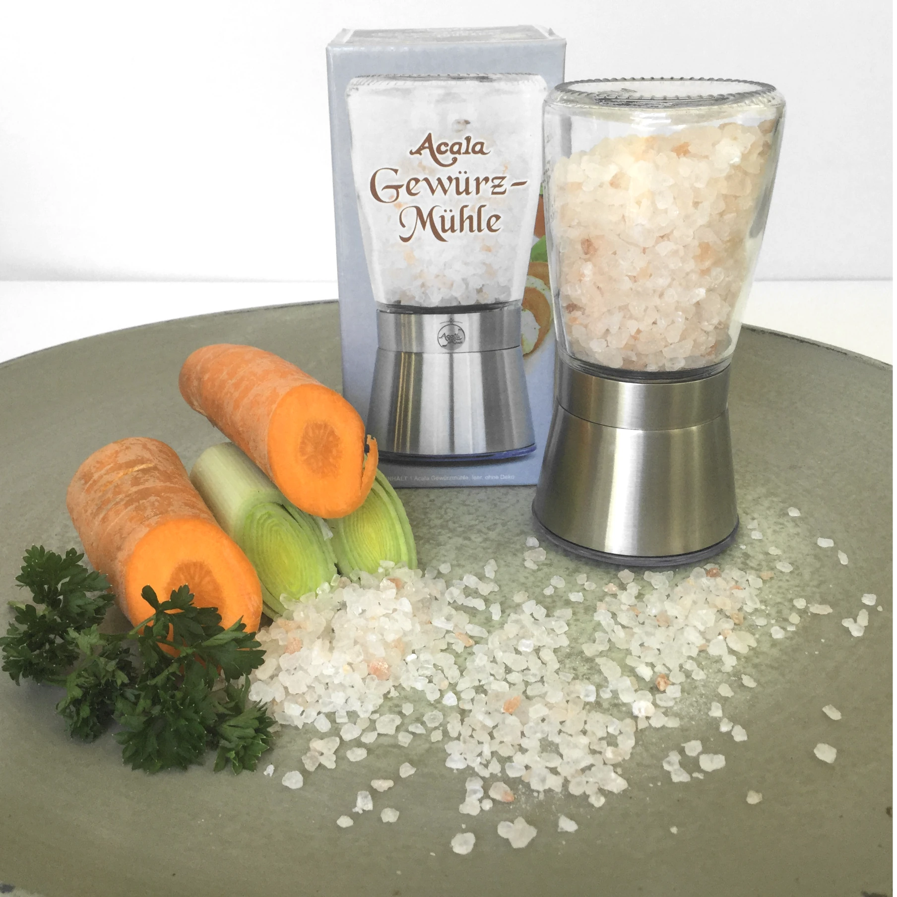 Auf einem Teller neben einer Salzmühle liegen Karotten und Sllerie, auf dem Teller ist Salz verteilt