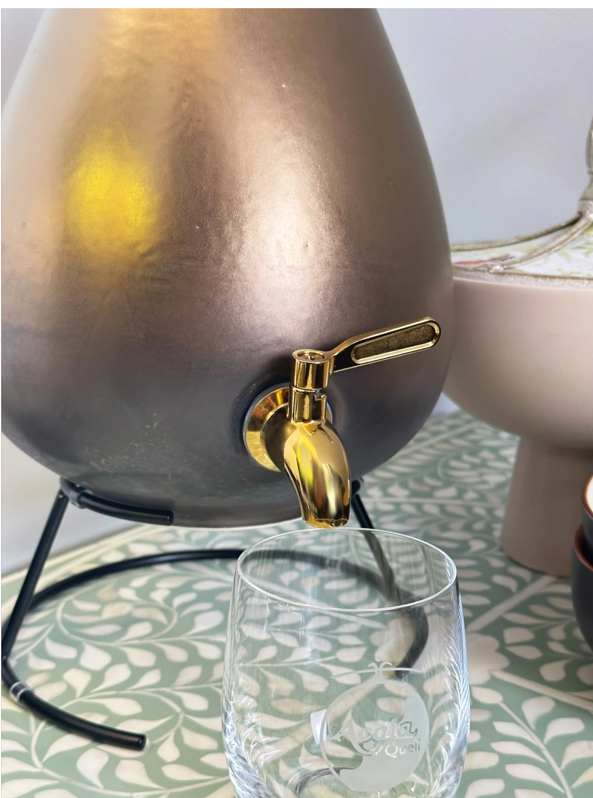 Wasserspender in Gold. mit goldenem Hahn. Vor dem Spender steht ein Hahn