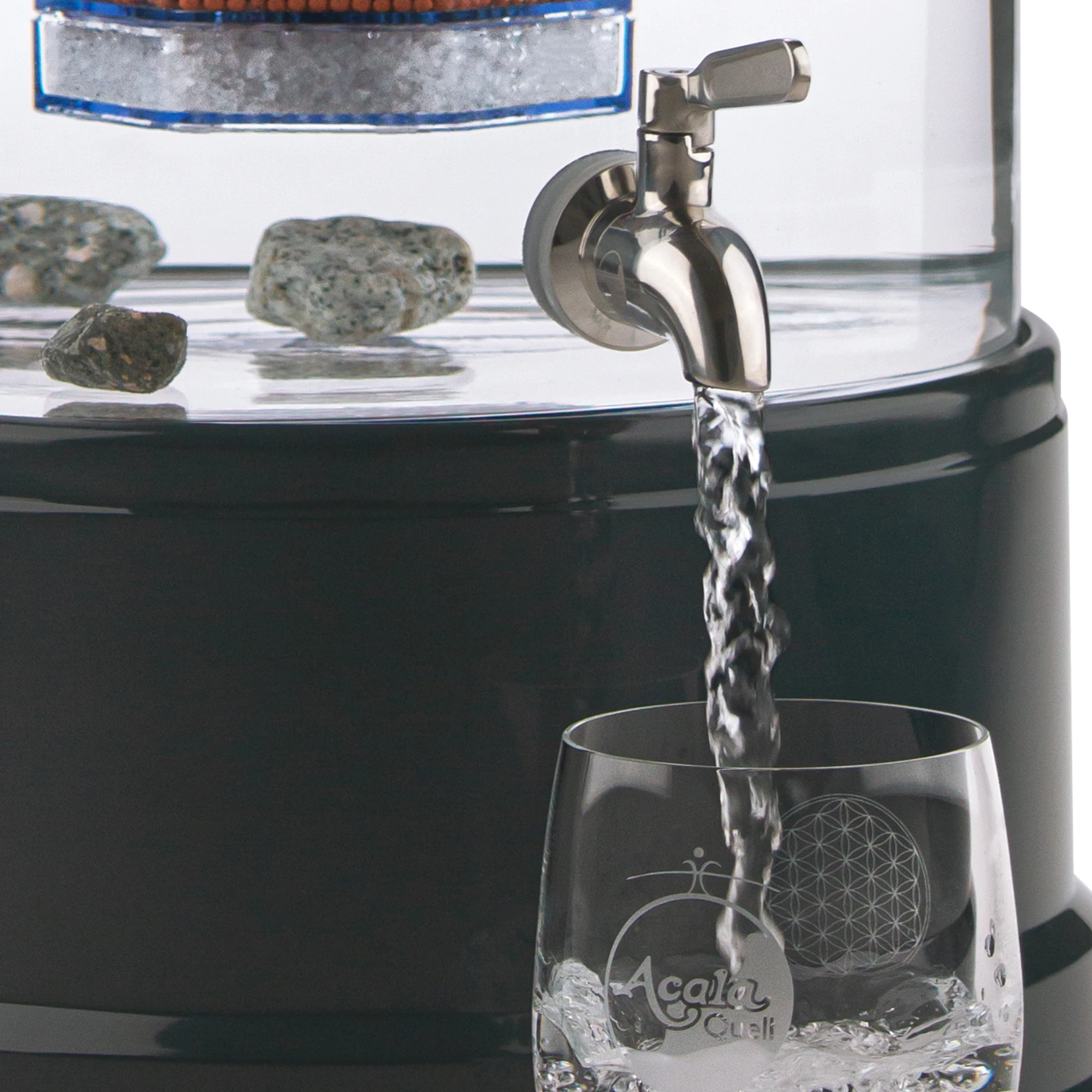 Zu sehen ist der Edelstahl Wasserhahn Yakawa für Standfilter an einem Glastank in kristallklar montiert. Der Hahn ist silber, man sieht das AcalaQuell Logo darauf. Der Hebel zum öffnen ist nach vorne gedreht, Wasser läuft in ein darunter stehendes Glas.