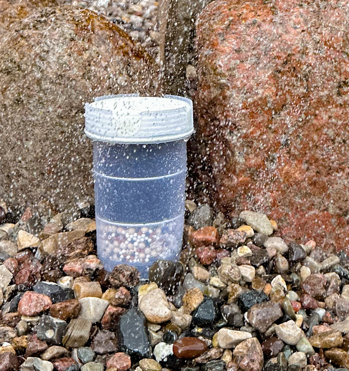 Filterkartusche für AcalaQuell Kannen Wasserfilter auf Steinbett vor zwei großen Steinen.