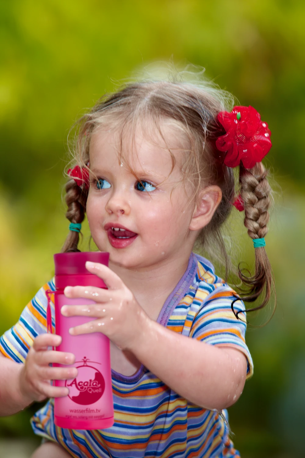 Zu sehen ist ein kleines Mädchen mit zwei seitlichen geflochtenen Zöpfen und Blumen darin. Sie ist circa zwei Jahre alt und hält eine pinke Easygo Tritan Trinkflasche in beiden Händen. 