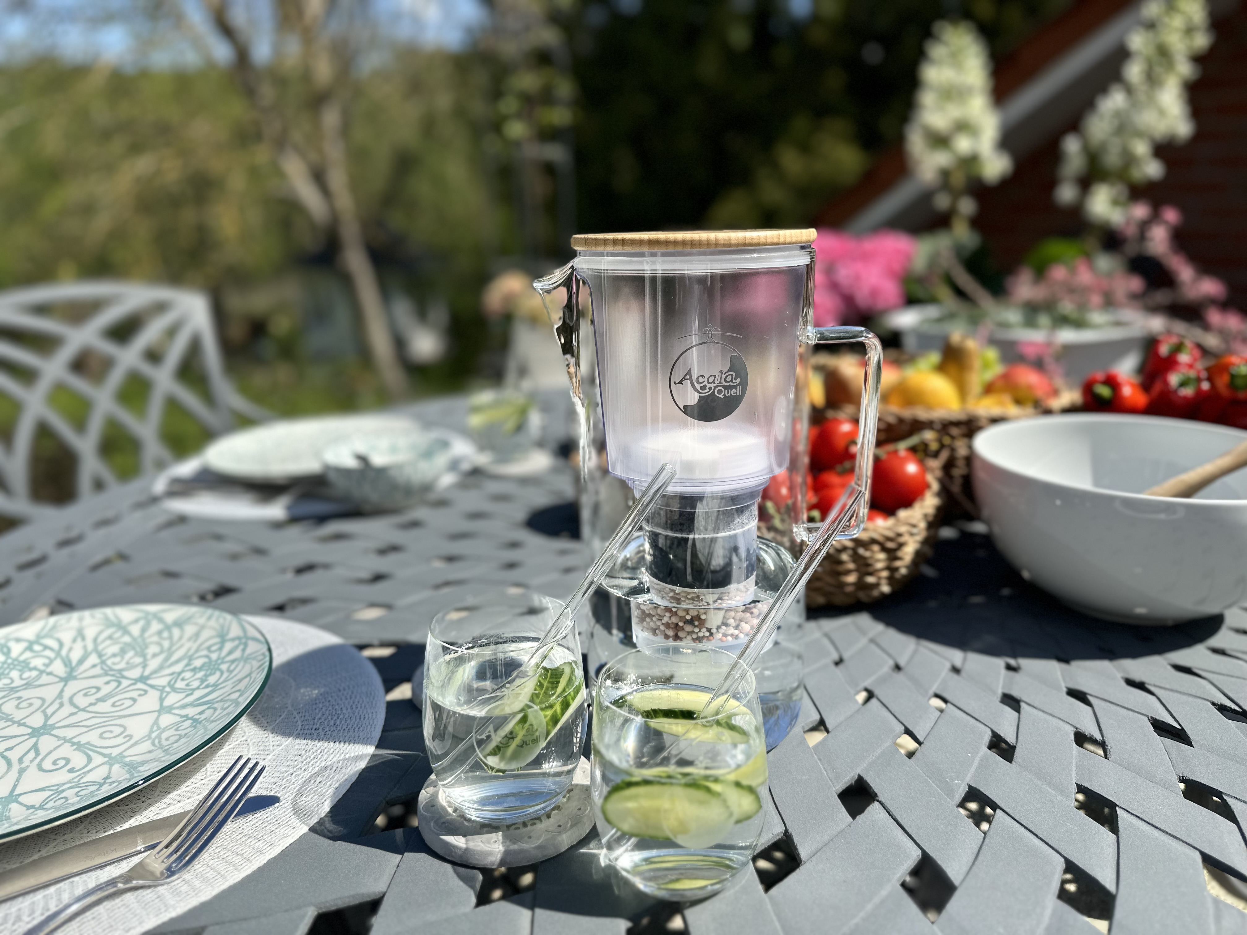 Zu sehen ist der Silizia Kannenwasserfilter aus Glas von Acala auf einem gedeckten Gartentisch. 