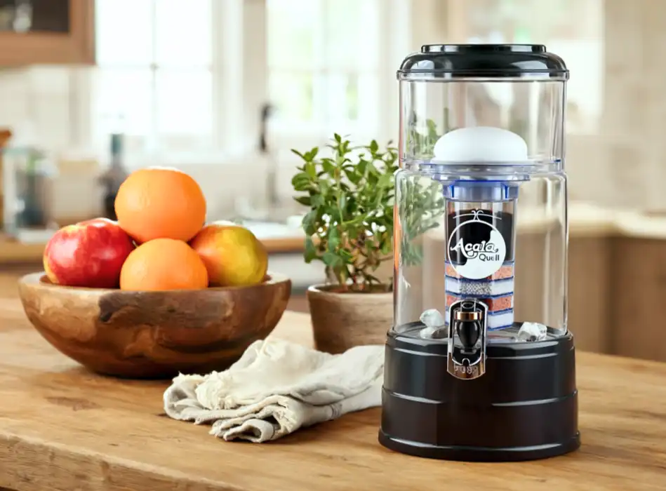 AcalaQuell Mini Wasserfilter mit kristallklarem 5-Liter-Glastank und anthrazitfarbenem Deckel und Sockel, auf einer Küchenarbeitsfläche stehend.