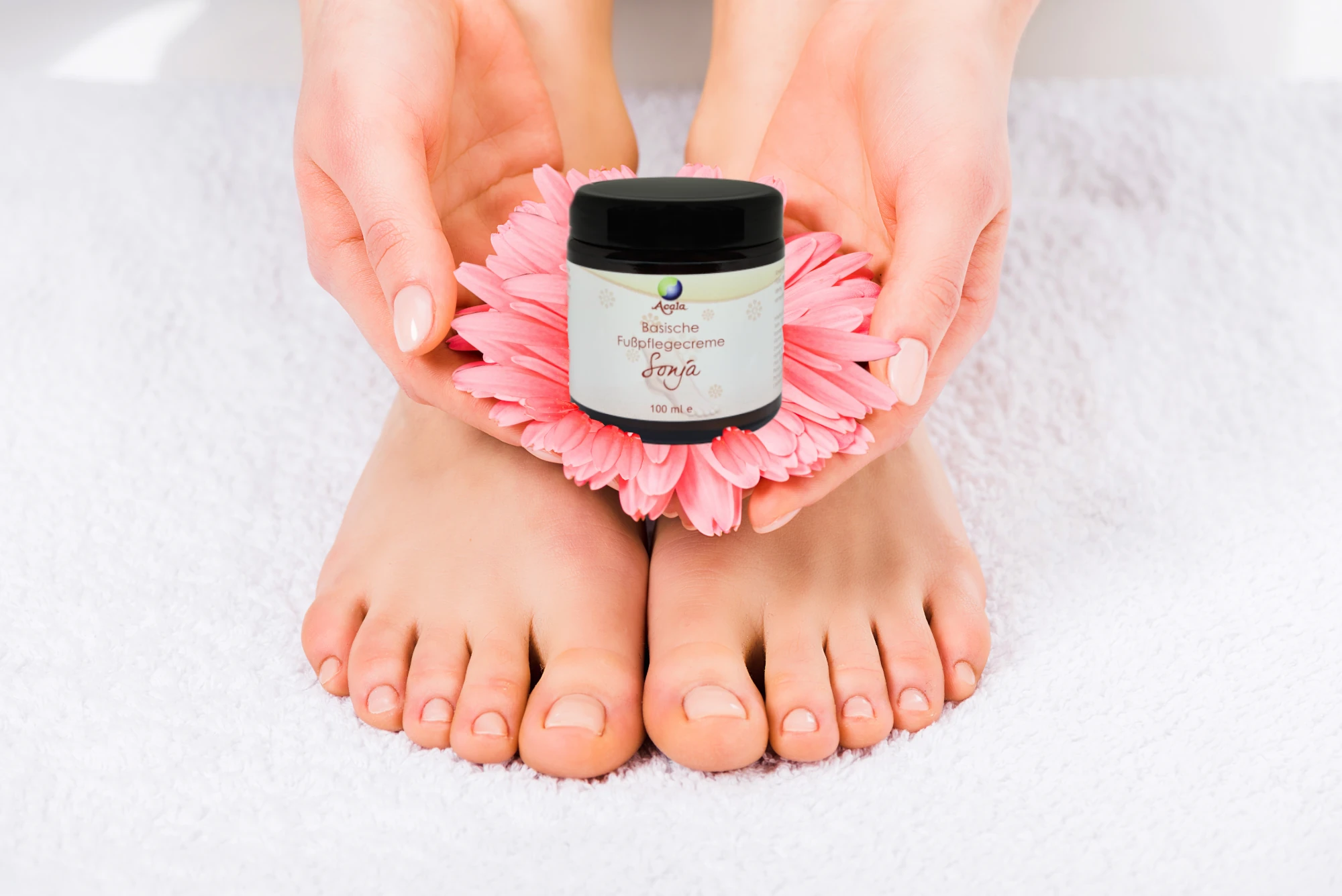 Das Bild zeigt Frauenfüße und Hände auf weißem Untergrund. Die Frau hält eine rosane Blüte in den Händen, auf der die Fußcreme steht. Zu sehen ist die Fußpflege Creme Sonja von Acala.