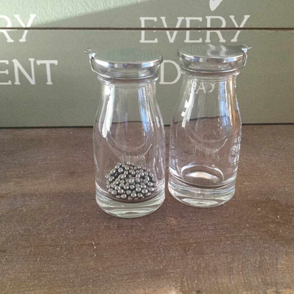Auf dem Bidl sind 2 kleine durchsichtige Flaschen mit Edelstahldeckel.In der linken Flasche sind Edelstahl-Reinigungskugeln und die rechte Seite zeigt wie eine gereinigte Flasche ausschaut Auf dem Bidl sind 2 kleine durchsichtige Flaschen mit Edelstahldeckel.In der linken Flasche sind Edelstahl-Reinigungskugeln und die rechte Seite zeigt wie eine gereinigte Flasche ausschaut