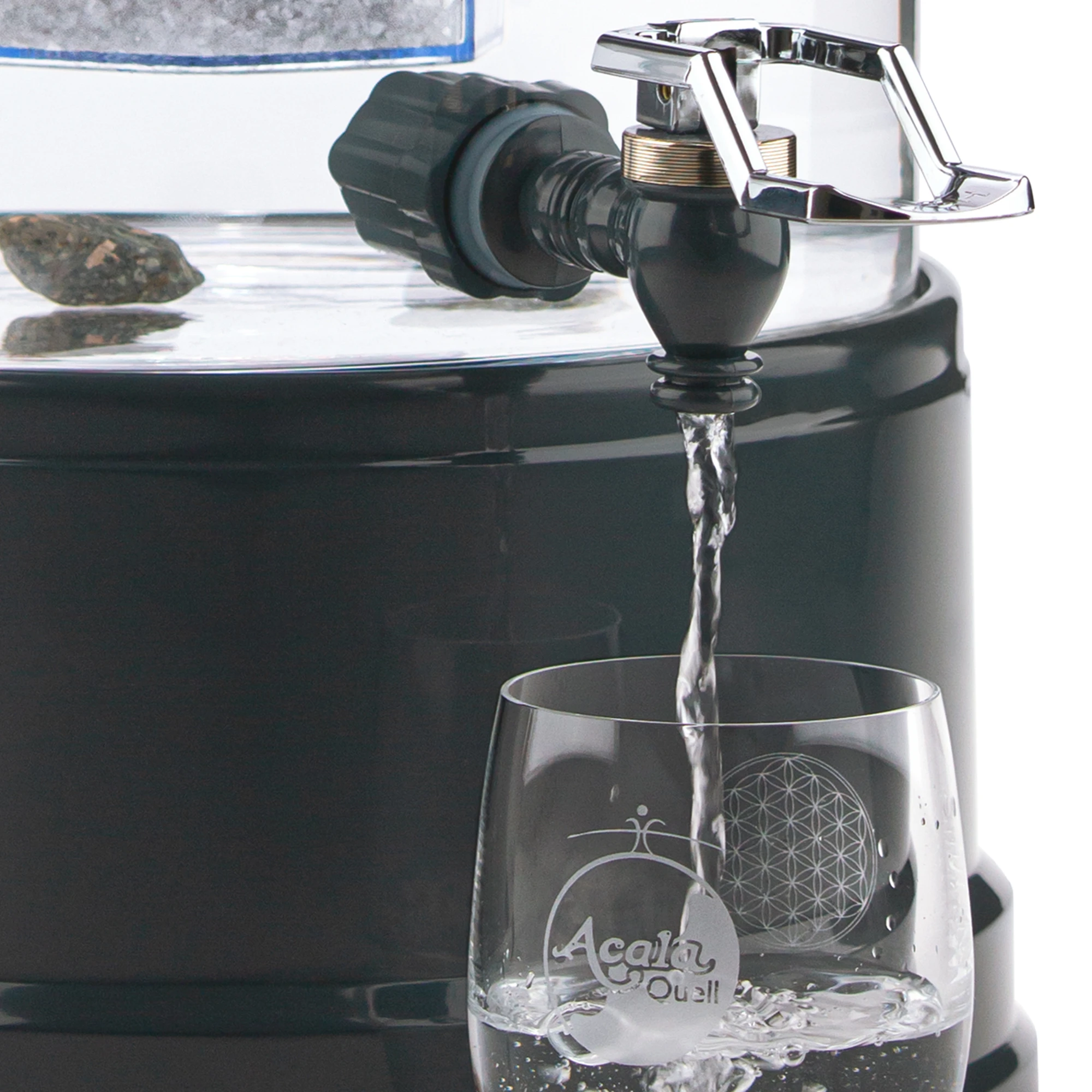 Zu sehen ist der Kunststoff Wasserhahn in anthrazit für Acala Stand Wasserfilter an einem Glastank in kristallklar montiert. Der silberne Bügel ist nach oben geklappt, Wasser läuft in ein Glas, welches darunter steht.
