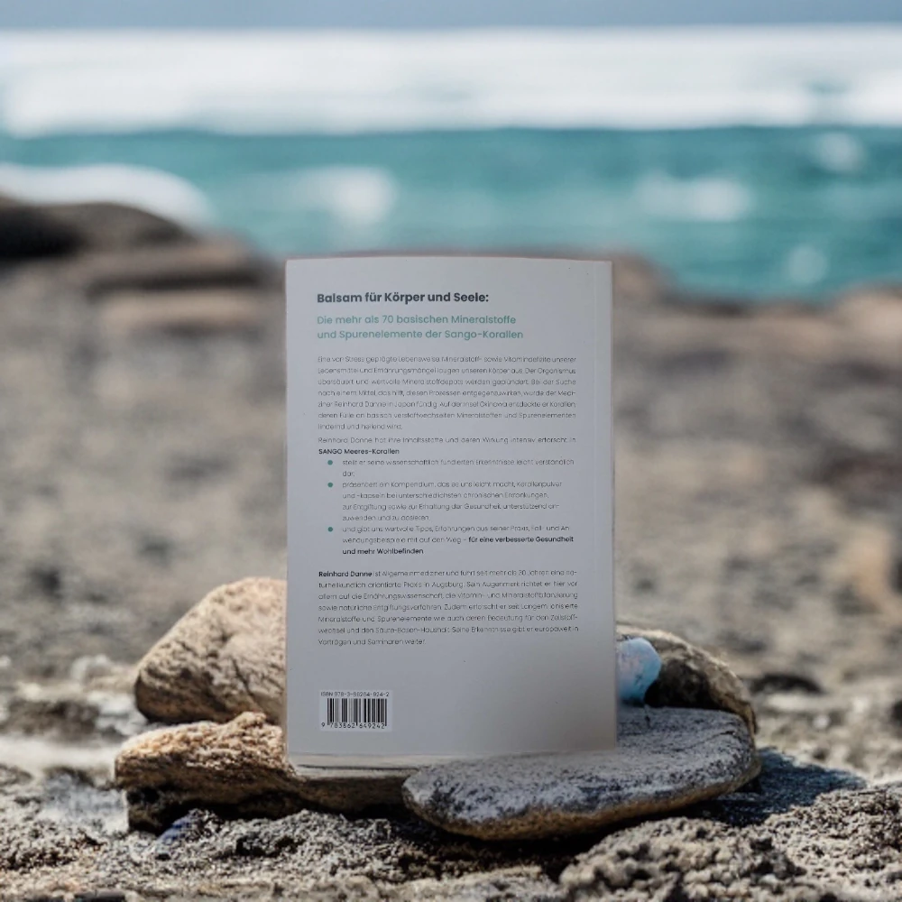 Zu sehen ist die Rückseite eines Buches über die Sango Koralle von Reinhard Danne an einem Strand.