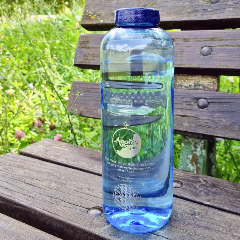 Eine blaue Tritan Trinkflasche Grip 1L mit dunkelblauem Schraubdeckel auf einer brauen Holzbank in einer Wiese.