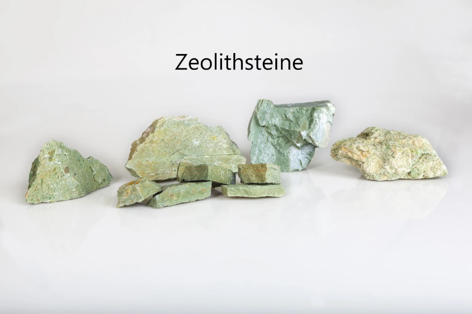 Mehrere grünliche beige Steine vor weißem Hintergrund. Darüber steht Zeolithsteine.