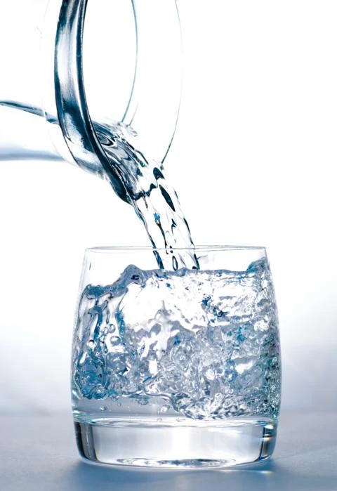 Wasser wird mit Schwung aus einer Flasche in ein Wasserglas gegossen.