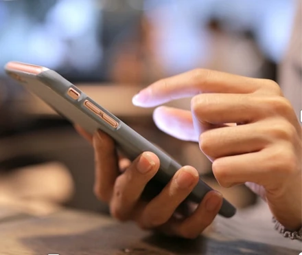 eine Hand hält das Smartfone, die ander tippte etwas ein.