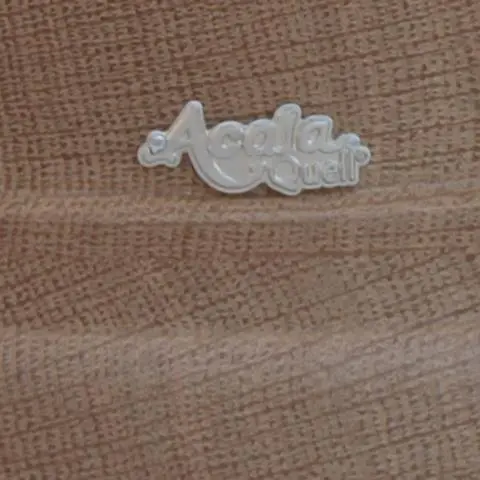 Zu sehen ist ein Großausschnitt eines Acala Echtholz Sockels aus Eiche mit dem schlichten, silbernen Acala Logo darauf. 