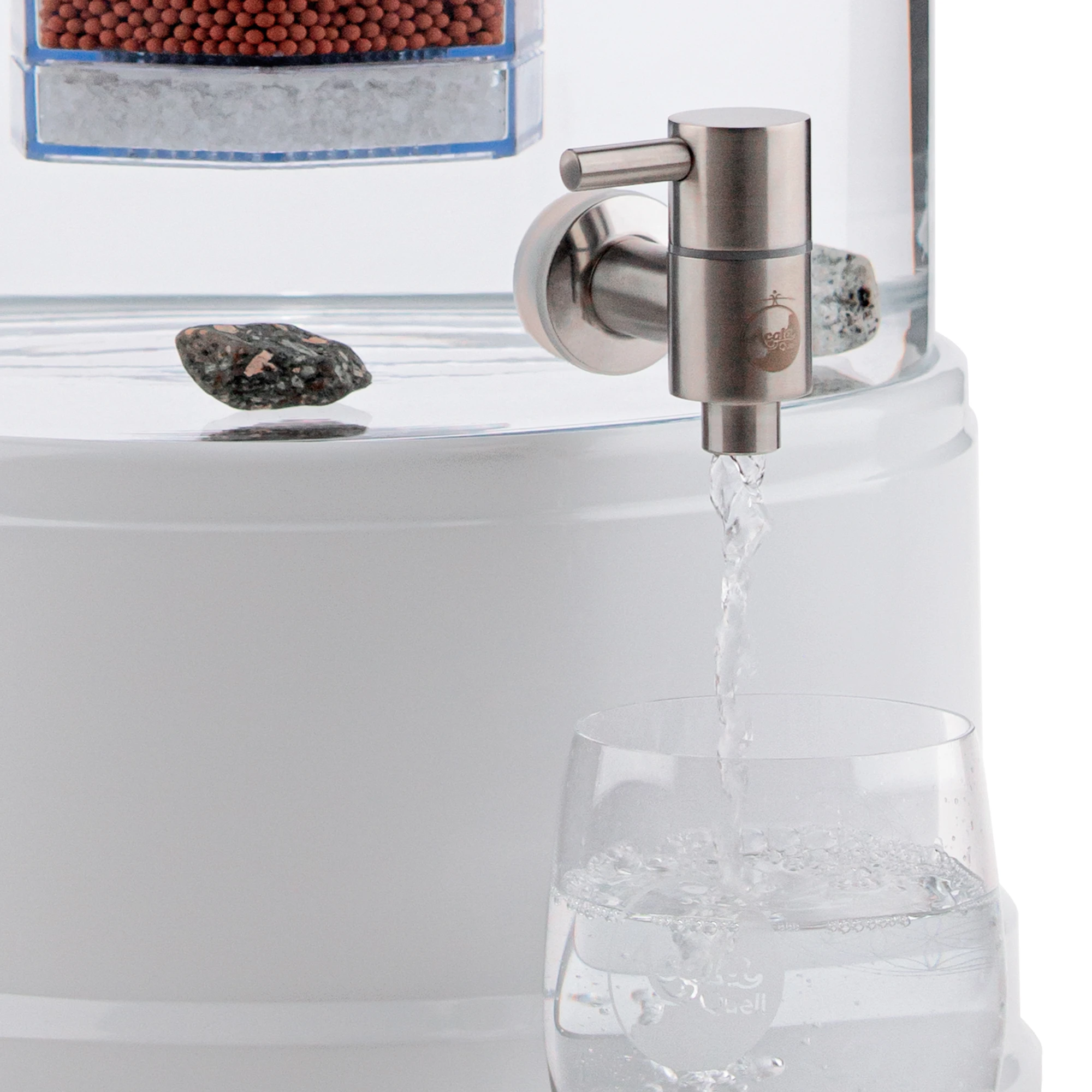 Zu sehen ist der Edelstahl Wasserhahn Makino für Standfilter an einem Glastank in kristallklar montiert. Der Hahn ist silber, man sieht das AcalaQuell Logo darauf. Der Hebel zum öffnen ist nach links gedreht, Wasser läuft in ein darunter stehendes Glas.