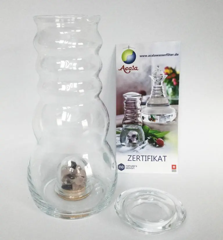 Zu sehen ist eine Glaskaraffe vor weißem Hintergrund. Der flache Glasdeckel liegt daneben und dahinter steht ein Zertifikat. Das Bild zeigt den Cadus Krug mit Glasdeckel und Zertifikat von Acala.