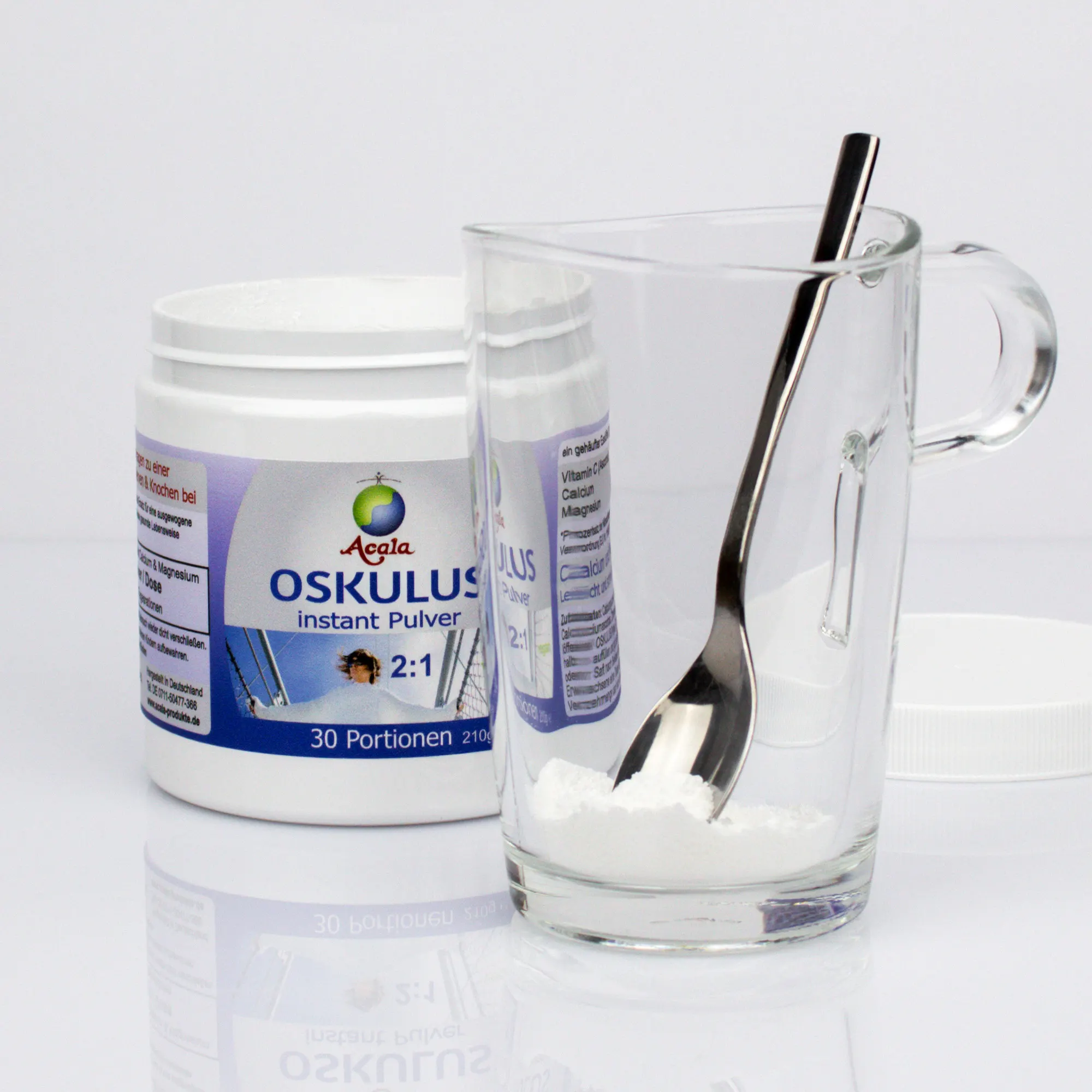 Links steht eine geöffnete Dose Oskulus 2:1. Rechts davor steht ein Glas mit einer Portion Oskulus-Pulver und einem Teelöffel darin. Im Hintergrund liegt rechts der weiße Schraubdeckel.