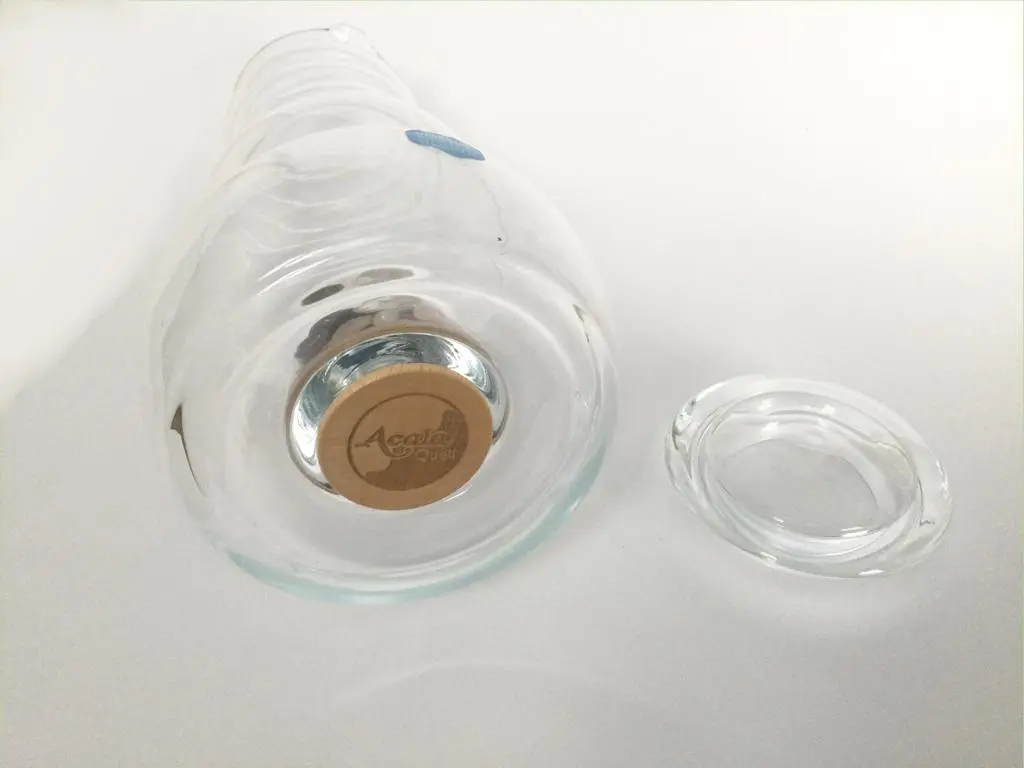 Man sieht die Bodenansicht auf den Holz-Verschlussdeckel mit Acala Logo von der Cadus Glas Karaffe. Der Glas Deckel der Karaffe liegt dabenen.