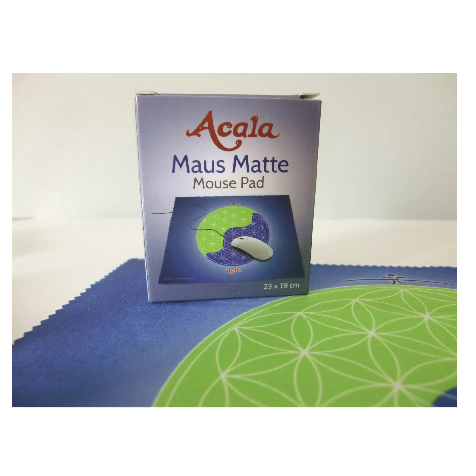 Zu sehen ist ein Teil der Acala Maus Matte, die auf einem hellen Tisch liegt. Auf der linken Ecke steht der Verpackungskarton.