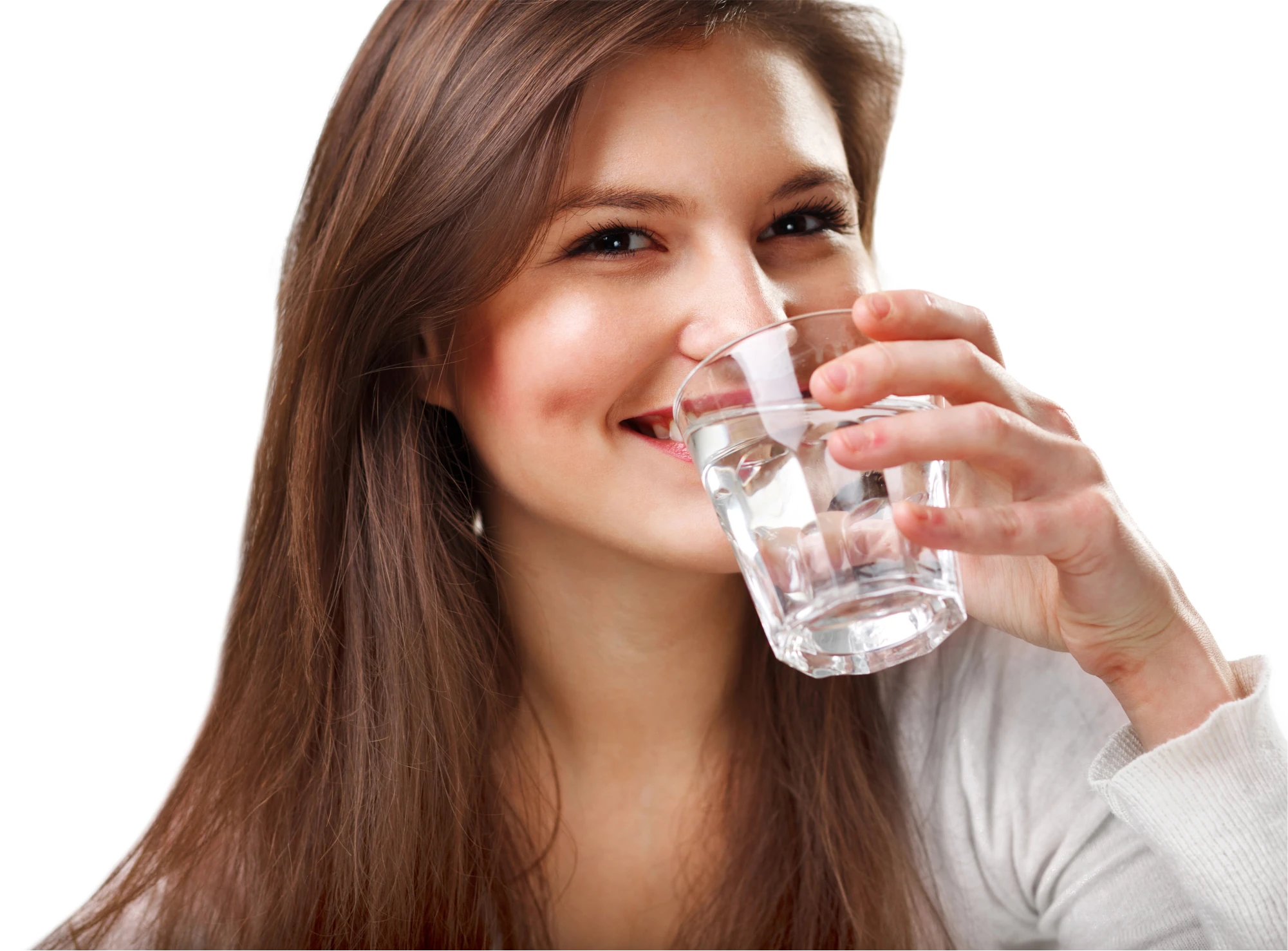 Junge Frau mit dunklen langen Haaren vor weißem Hintergrund will Wasser aus einem Glas trinken, sie lächelt.