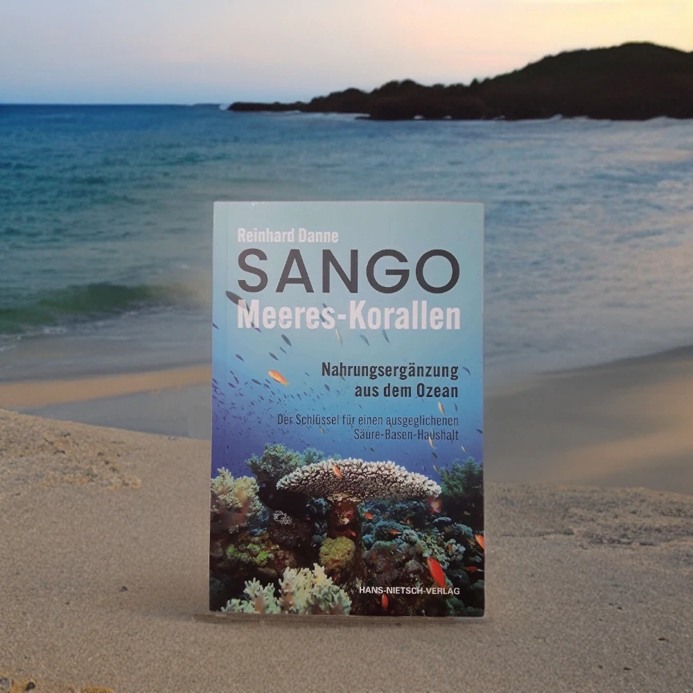 Sango Meeres-Korallen: Nahrungsergänzung aus dem Ozean Zu sehen ist ein Buch über die Sango Koralle von Reinhard Danne an einem Strand.