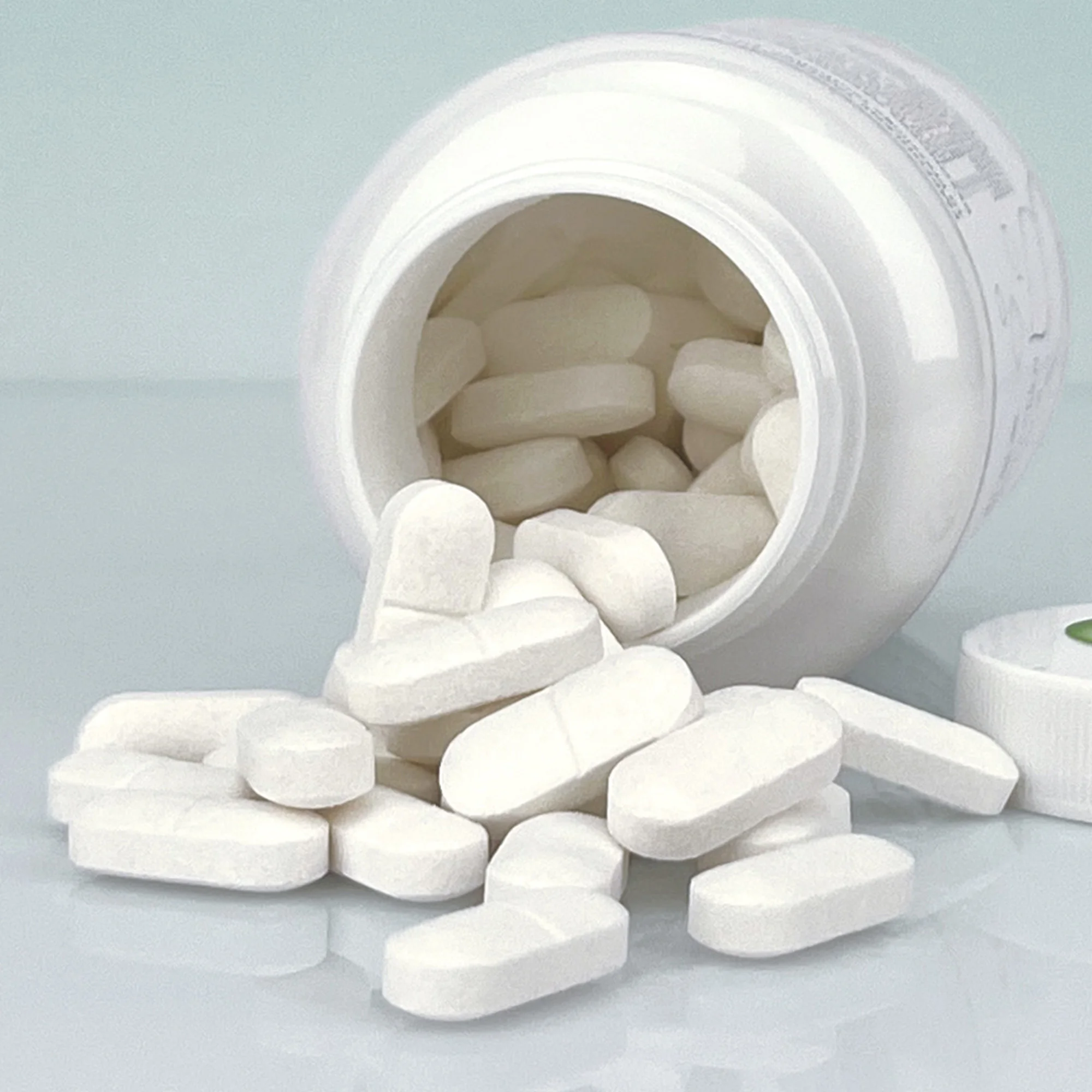  liegende und geöffnete weiße Dose auf einem weißen Tisch und vor weißem Hintergrund. Man kann in die Dose hineinschauen, dort und vor der Dose liegen weiße Moretties-Presslinge.