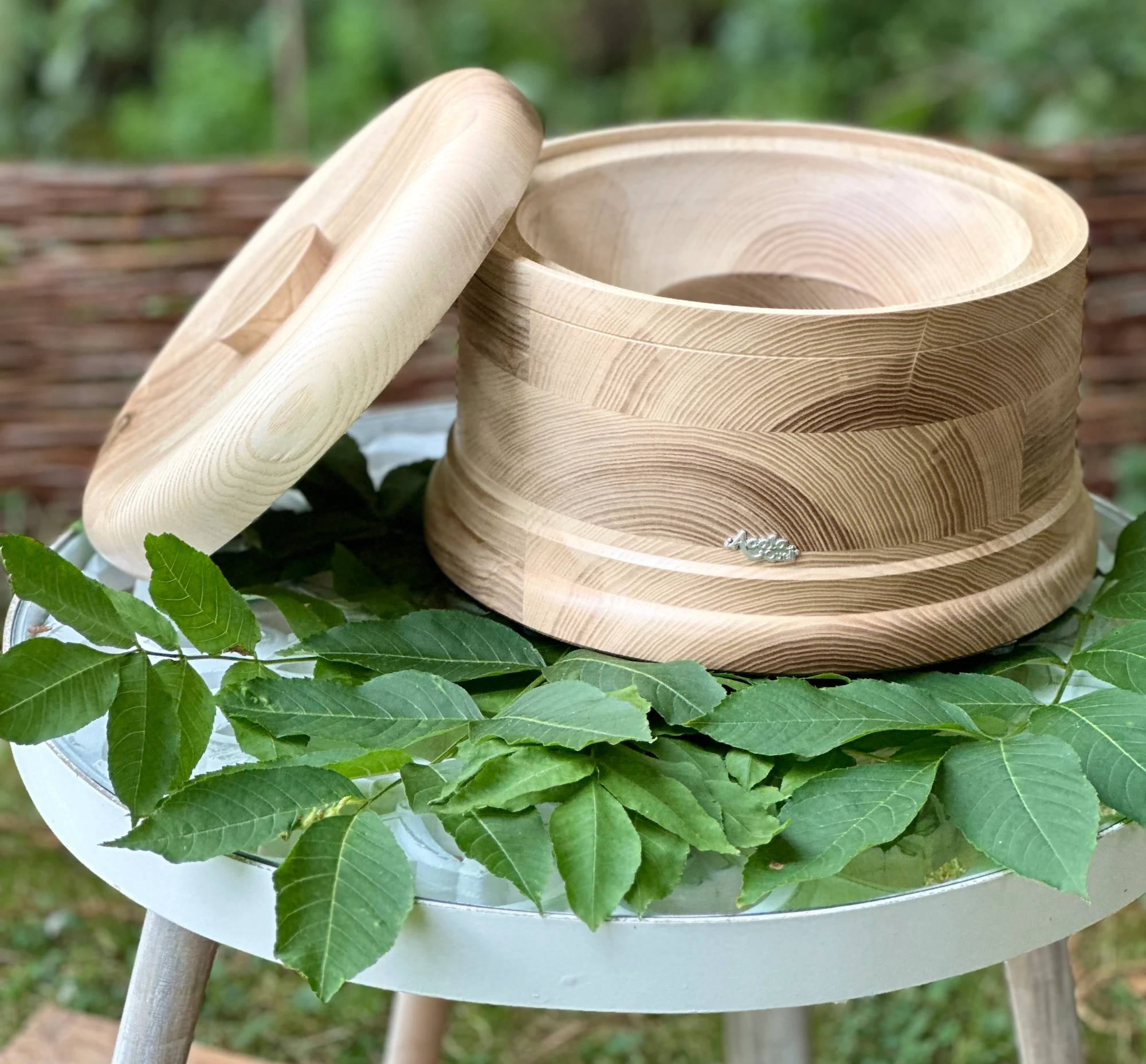 Echtholz Sockel und Deckel aus Esche für AcalaQuell Stand Wasserfilter auf einem Tisch im grünen Garten.