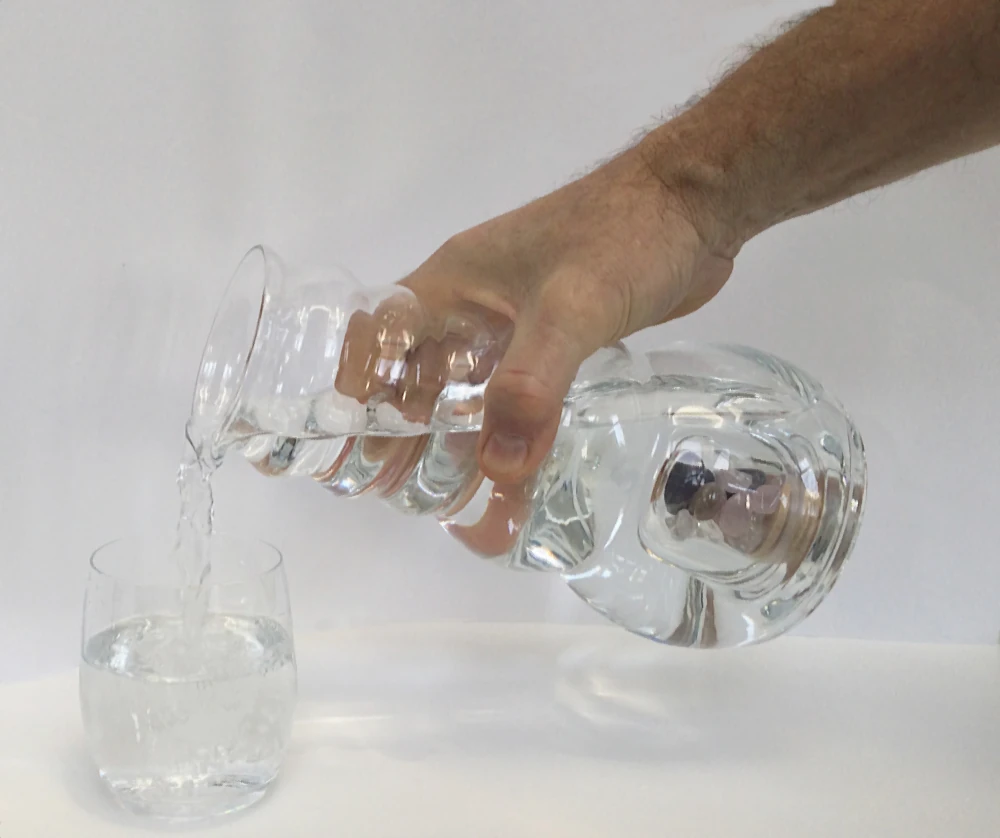 ein Glas und eine Cadus Karaffe ,ein hand gießt wasser aus der Karaffe in das Glas männliche Hand gießt Wasser aus dem Acala Cadus Krug in ein Trinkglas