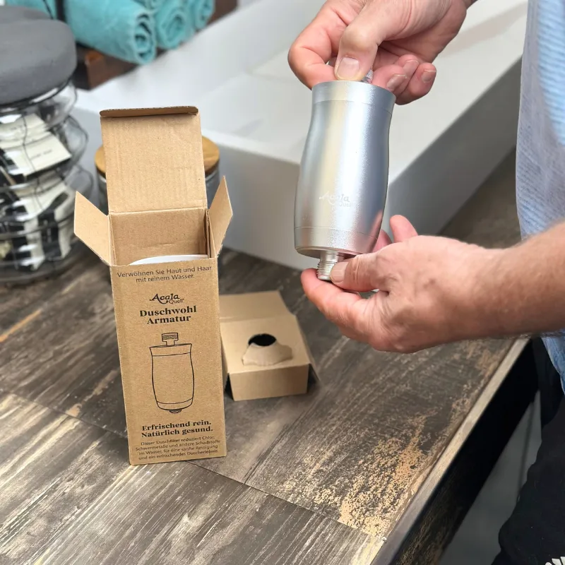 Ein Mann hat gerade die den Duschfilter oder auch wasserfilter für die Dusche ausgepackt und hält ihn in der Hand