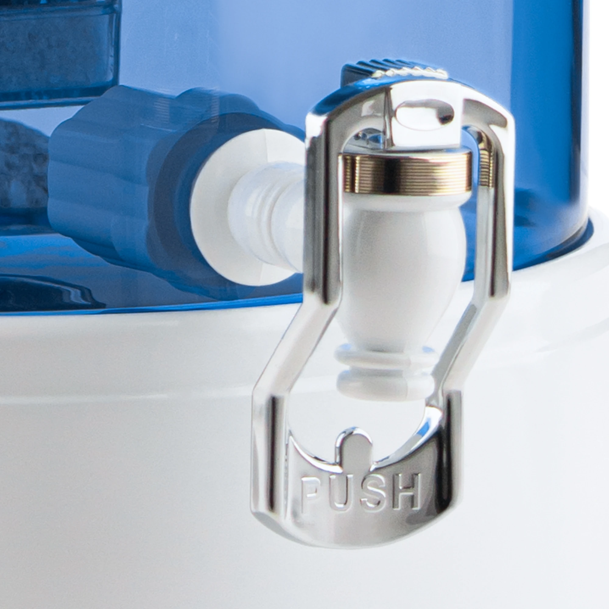 Zu sehen ist der Kunststoff Wasserhahn in weiß für Acala Stand Wasserfilter an einem Glastank in blau montiert. Der Hahn hat einen großen Bügel in silber auf dem das Wort Push in silbernen Großbuchstaben zu lesen ist.