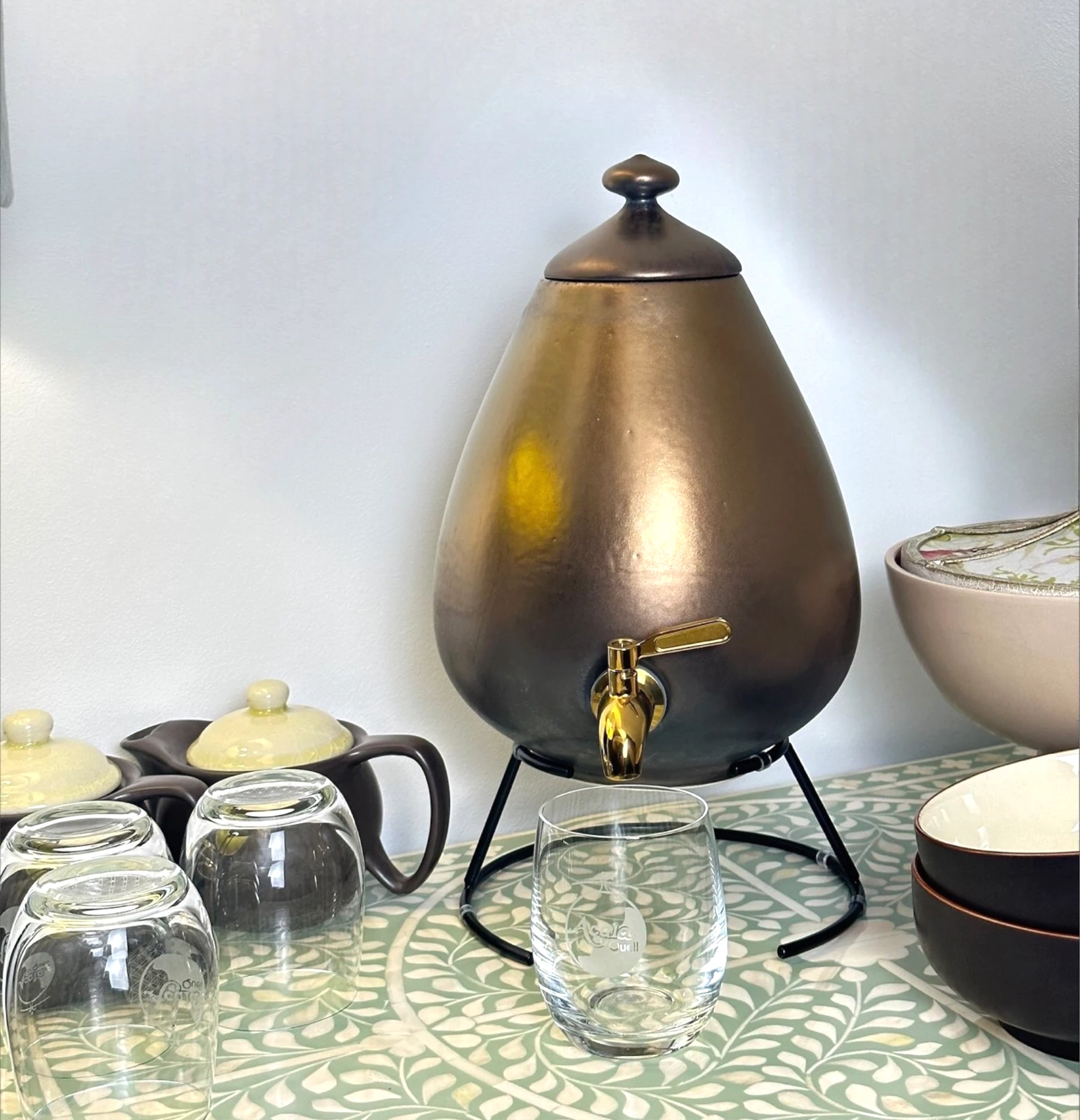 Wasserspender in gold,links daneben stehen Gläser