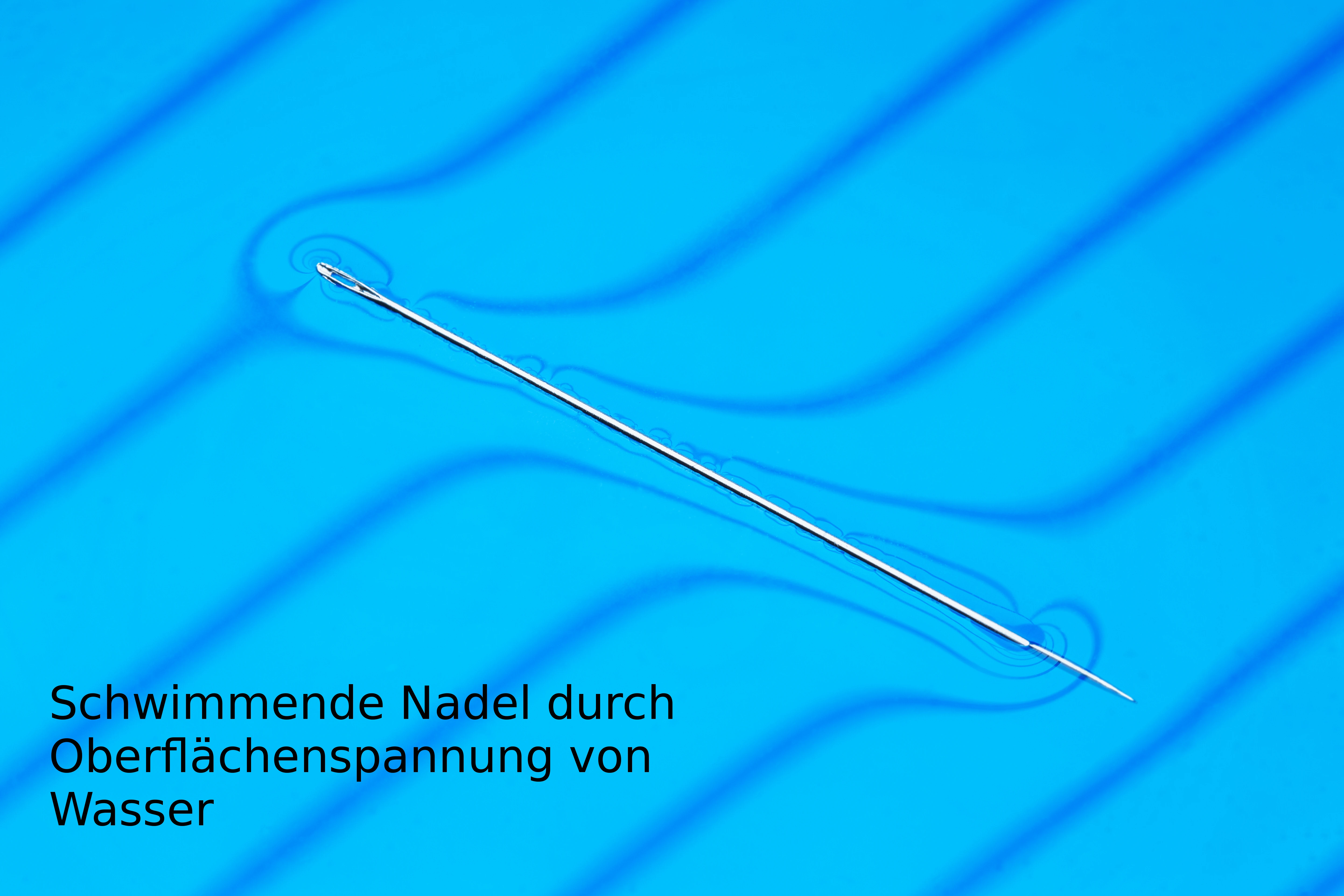 Zu sehen ist eine Nähnadel, die auf der Wasseroberfläche schwimmt. Durch die Oberflächenspannung des Wassers sinkt sie nicht.