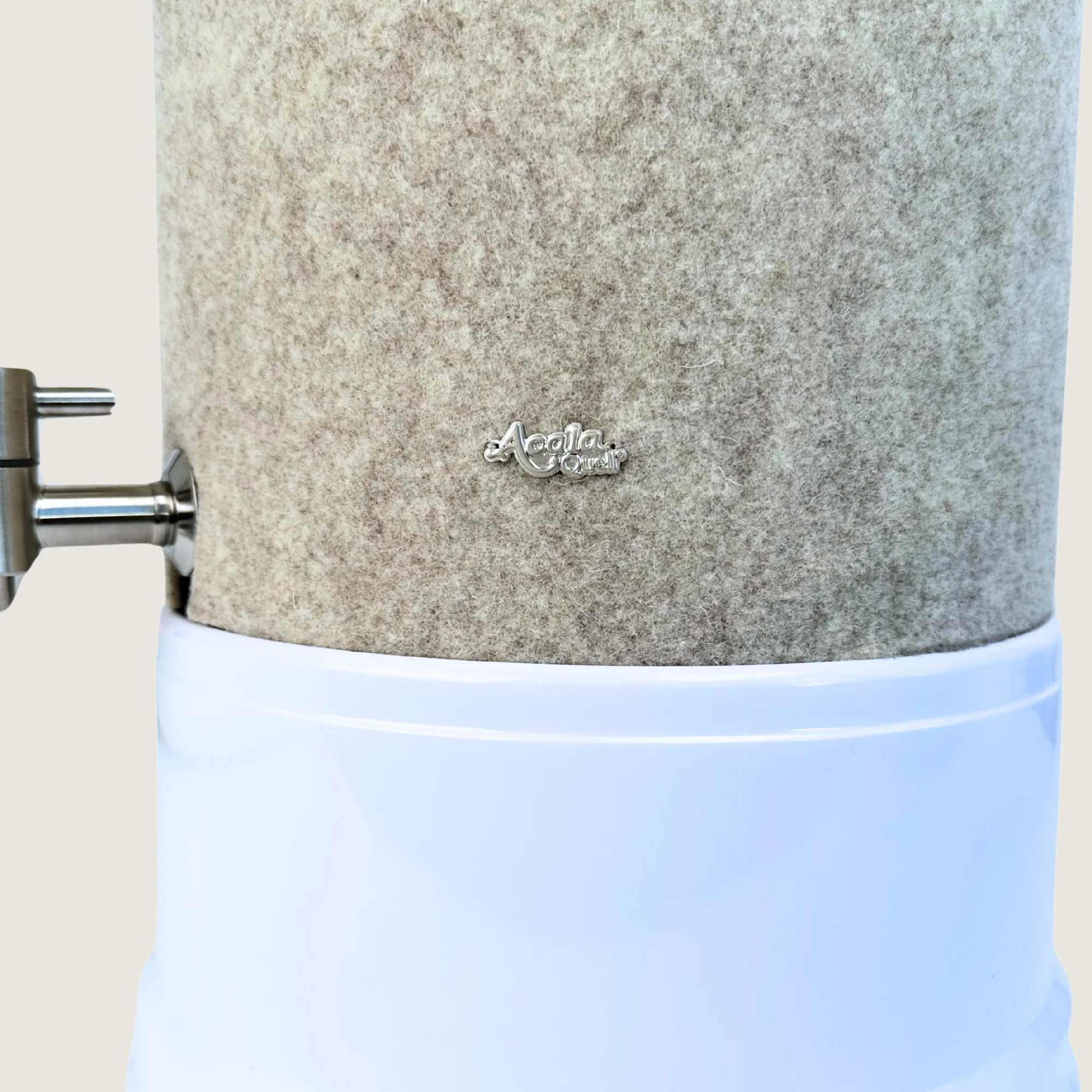 Ausschnitt eines Stand Wasserfilters von Acala mit Sockel in weiß, Edelstahl Wasserhahn Makino und Schurwolle Lichtschutz in beige.