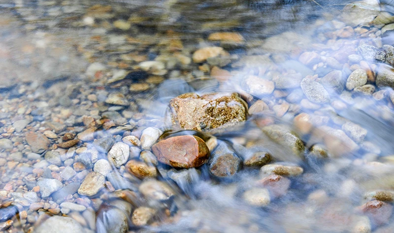 auf dem bild ist ein Kiesbett zu sehen über das klares Wasser fließ