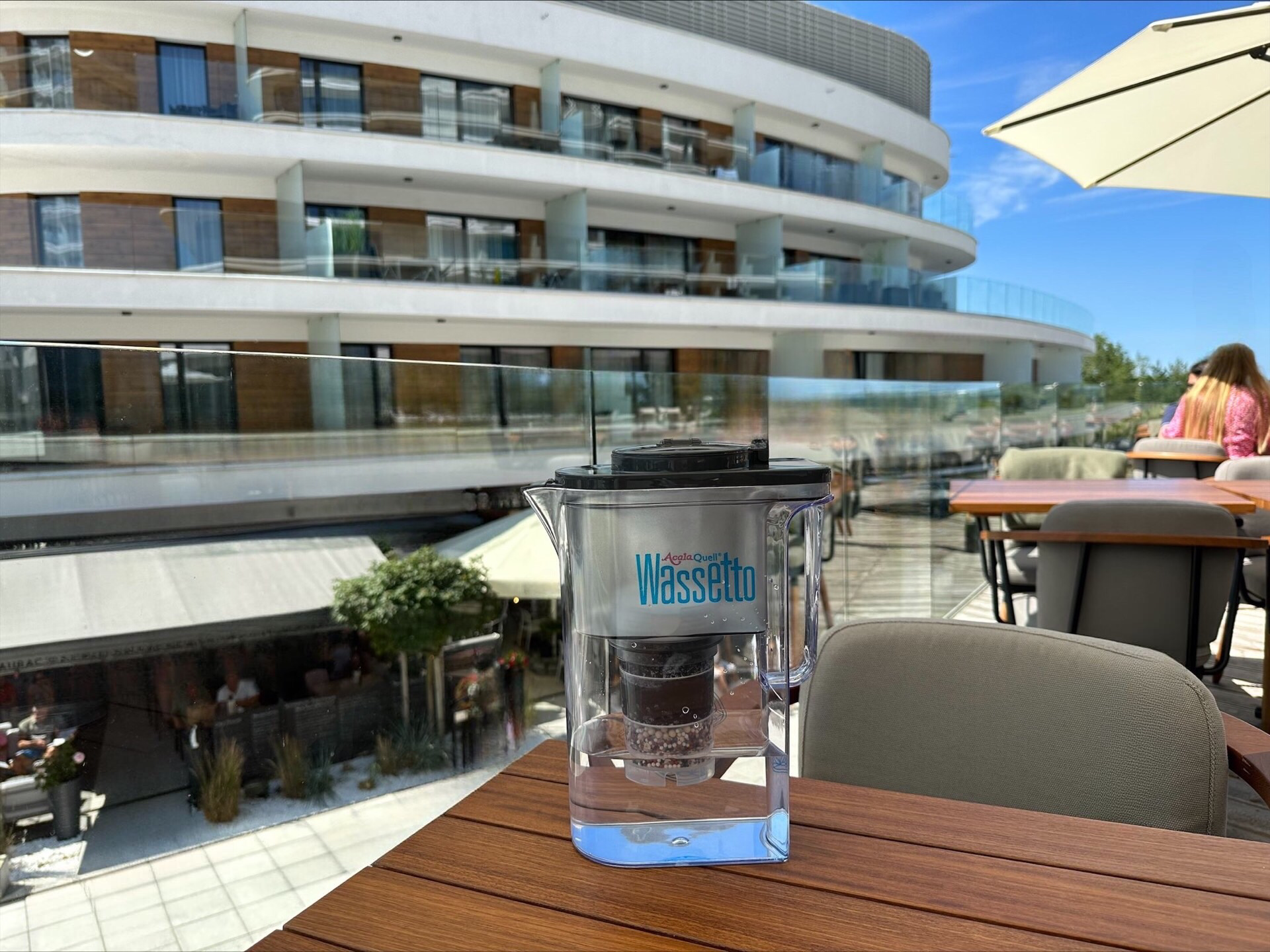 Wassetto Kannen Wasserfilter auf einem Holztisch. Im Hintergrund sieht man einen Hotelkomplex und strahlend blauen Himmel.