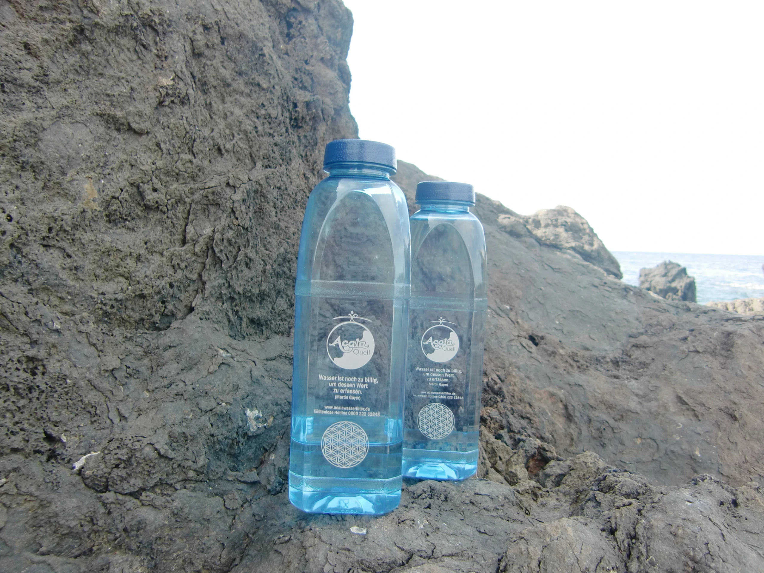 2 8 Kantige Tritanflaschen stehen, halb mit Wasser gefüllt, auf einem Felsen