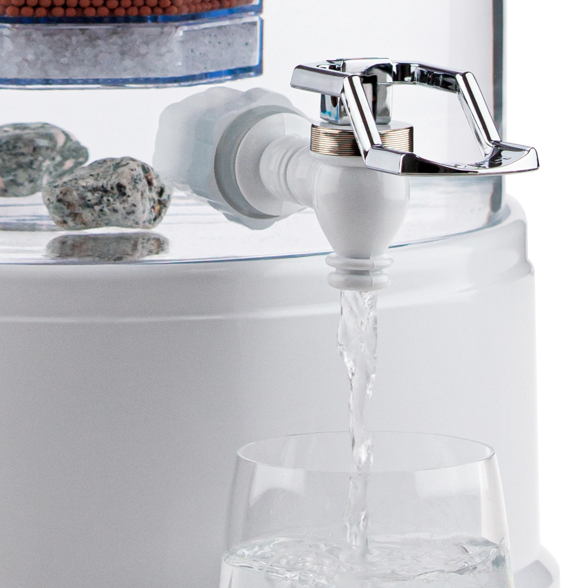 Zu sehen ist der Kunststoff Wasserhahn in weiß für Acala Stand Wasserfilter an einem Glastank in kristallklar montiert. Der silberne Bügel ist nach oben geklappt, Wasser läuft in ein Glas, welches darunter steht.