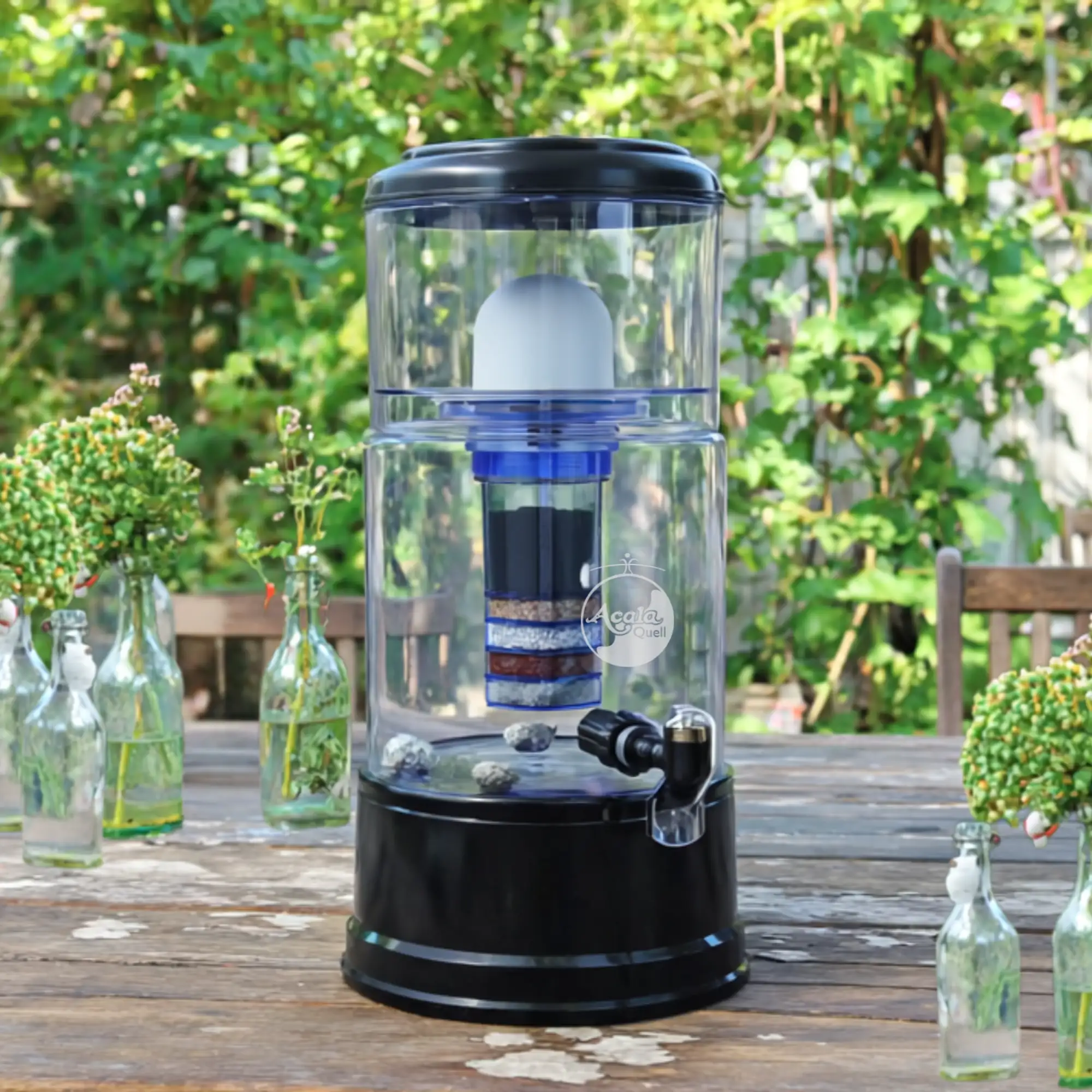 Wasserfilter mit Glastank und anthrazitfarbenem sockel und Deckel im Garten auf einem Tisch
