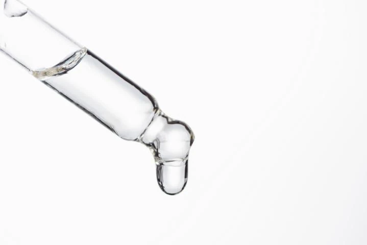 Zu sehen ist der vordere Teil einer Pipette aus der sich grade ein Tropfen Flüssigkeit löst, weißer Hintergrund. Das Bild gehört zum Acala Blog Wassertropfen.